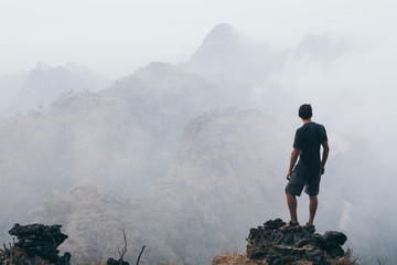 Man standing on the rock overlooking tropical mountains at sunrise foggy morning in Hpa-an, Myanmar