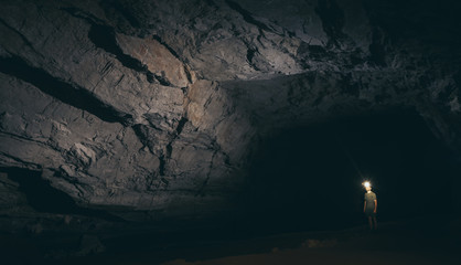 Human silhouette stands inside water cave with torch in hand in Konglor, Laos
