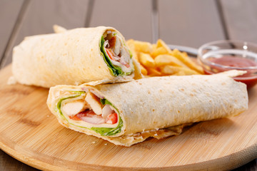 Wrapped sandwich chicken tortilla with fried potatoes and dipping sauce on wooden plate , wood background.