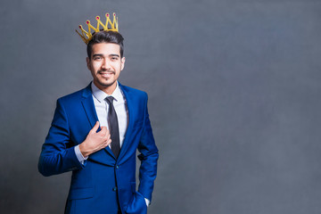Attractive smiling man with a crown on his head on a gray background.