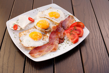 Healthy bacon fried egg on toast bread breakfast on plate , fresh tomatoes and cheese on plate , wood background.