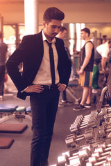 Businessman in suit near the stand with dumbbells in the gym.