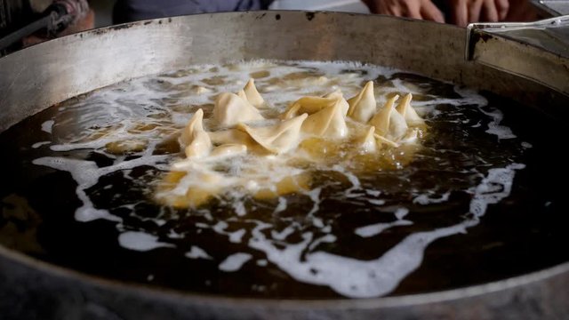 A man putting samosas in a huge container of oil to get deep fried . 