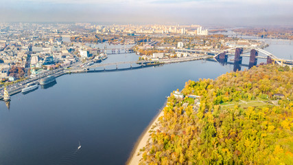 Fototapeta premium Aerial drone view of autumn pedestrian Park bridge, yellow fall trees, Truhaniv island, Dnieper river and Kyiv cityscape from above, city of Kiev, Ukraine