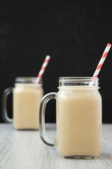 Peanut butter banana smoothie in glass jar mugs, side view. Copy space.