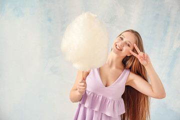 Beautiful woman with cotton candy showing victory gesture on light background