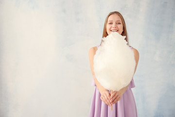 Beautiful woman with cotton candy on light background