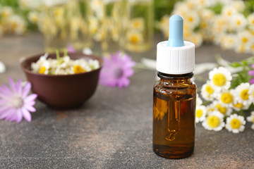 Fototapeta na wymiar Bottle of essential oil with wild flowers on grey table