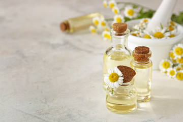 Bottles of essential oil with chamomile flower on light table