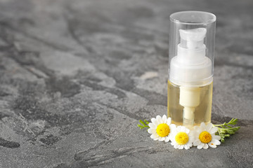 Bottle of essential oil with chamomile flowers on grey background