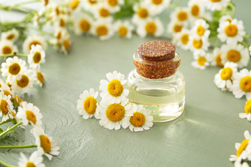 Fototapeta na wymiar Bottle of essential oil with chamomile flowers on wooden table