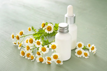 Fototapeta na wymiar Bottles of cosmetic product with chamomile flowers on wooden table