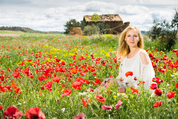 Obraz na płótnie Canvas Beautiful young female in white dress in poppy field of wild flowers