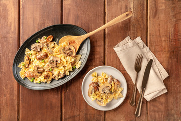 Mushroom pasta. Farfalle with cremini and green peas, shot from the top on a dark rustic wooden background