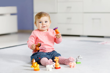 Adorable baby girl playing with domestic toy pets like cow, horse, sheep, dog and wild animals like giraffe, elephant and monkey. Happy healthy child having fun with colorful different toys at home