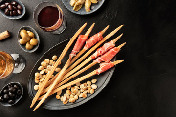 Italian antipasti. Prosciutto-wrapped Italian grissini with olives, almonds, and wine, shot from the top on a black background with a place for text