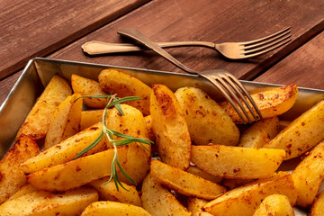 Potato wedges, oven roasted with rosemary, in a baking tray on a dark rustic wooden background