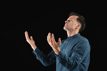 Religious man praying to God on dark background