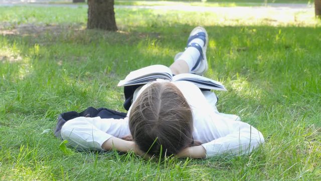 girl of school age reading a book lying on the grass, lying on her back with a book and dreaming. education