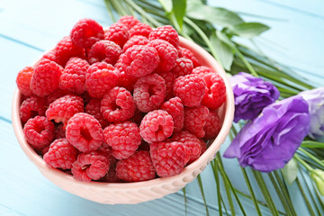 Bowl with ripe raspberry on wooden background