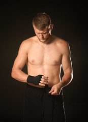 Fototapeta na wymiar Strong male boxer applying wrist bands against dark background