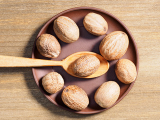 Spice Nutmeg (Myristica fragrans) on a brown clay plate on a wooden background with spoon
