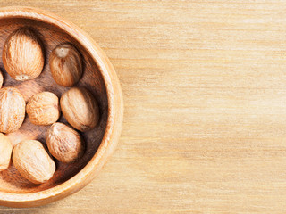 Spice Nutmeg (Myristica fragrans) in a wooden cup on a wooden background with copy space