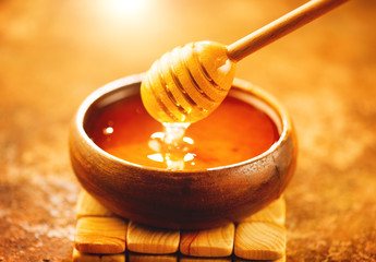Honey dripping from honey dipper in wooden bowl. Healthy organic thick honey pouring from the...