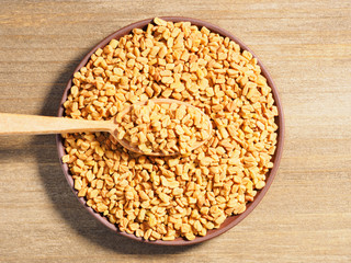 Fenugreek (Trigonetla) spice as background with wooden spoon