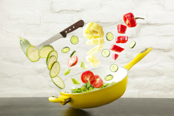 Fresh vegetable slices flying into a yellow pan. Healthy food or diet eating concept. Flying food. Meal preparation concept.