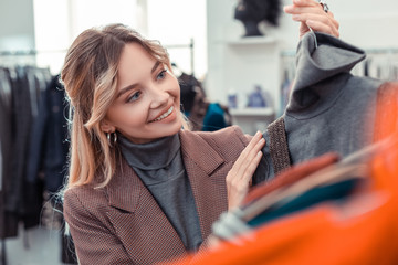 Blonde appealing woman smiling while choosing new outfit