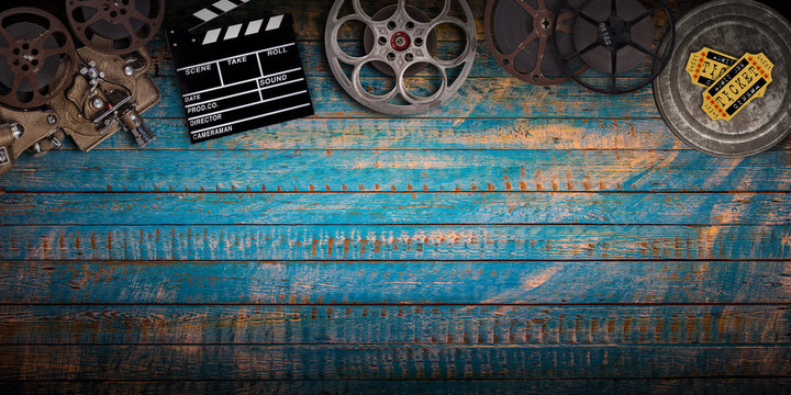 Cinema concept of vintage film reels, clapperboard and projector on old wooden background.