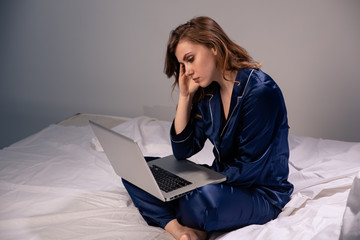 Tired handsome female sitting at home in the bed and working on a computer at night. Insomnia...