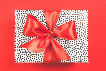 Gift box with black spots and red satin bow on a red background. Festive concept.