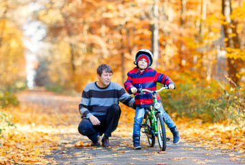 Little preschool kid boy and his father in autumn park with a bicycle. Dad teaching his son biking. Active family leisure. Child with helmet on bike. Safety, sports, leisure with kids concept