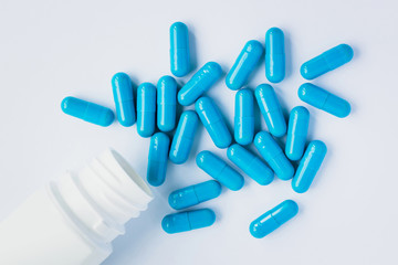 Blue capsules, pills on a light blue background. Capsules in a white jar. Vitamins, nutritional supplements for women's health