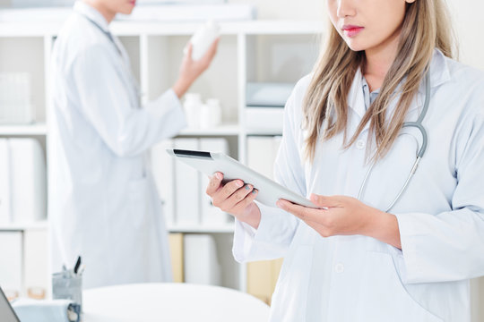 Cropped image of serious young female doctor reading information on screen of digital tablet