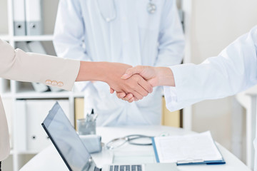 Fototapeta na wymiar Doctor shaking hand of female patient over office table with opened laptop, selective focus