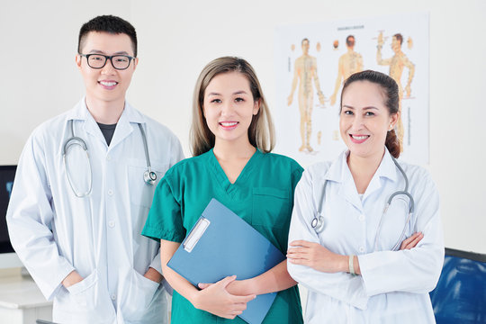 Team of smiling Vietnamese general practitioner, syrgeon and orthopedic surgeon standing in modern medial office