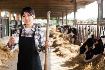 Cheerful woman is holding glass of milk at the cow farm