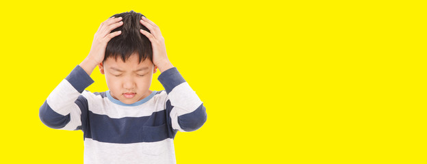 Asian child boy feel angry and stressed. He wearing a blue-grey T-shirt isolated on yellow background. His hand touching his head Pose.