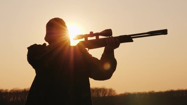 Silhouette of the hunter takes aim at the optical sight at sunset