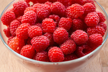 ripe red raspberries in a glass bowl on a wooden background as a natural background