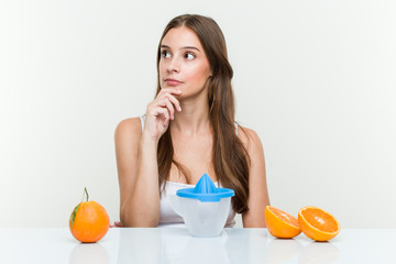 Young caucasian woman with an orange juicer looking sideways with doubtful and skeptical expression.