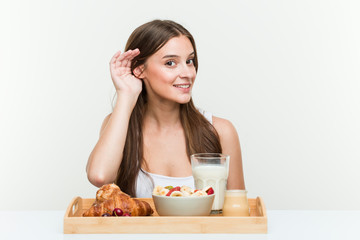 Young caucasian woman having breakfast trying to listening a gossip.