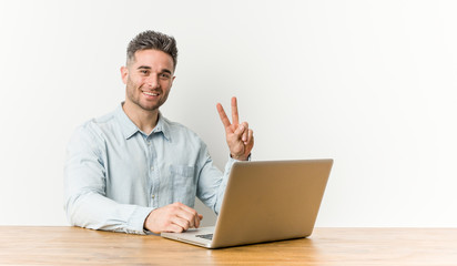 Young handsome man working with his laptop showing victory sign and smiling broadly.