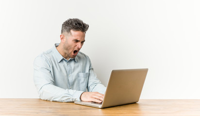 Young handsome man working with his laptop screaming very angry and aggressive.