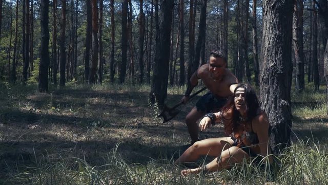 Muscular barbarian man grabs a woman by her hair, in the forest