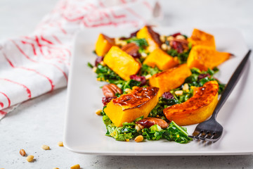 Pumpkin salad with nuts, cranberries and kale in a rectangular plate.
