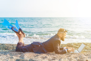 Successful businessman wearing snorkeling tools is working on the beach with laptop
